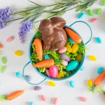 Close-up of Easter basket with chocolate bunny, mini carrots, and candy eggs on white background