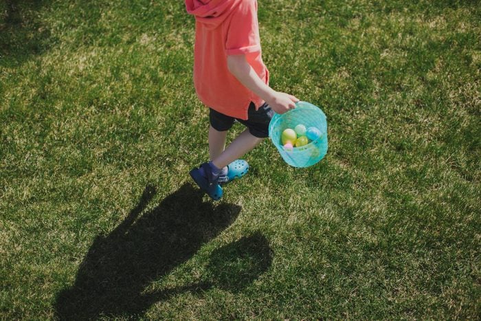 Little boy carries a bucket and fills it with Easter eggs on an Easter egg hunt.