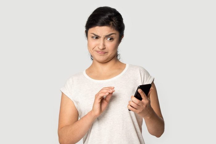 woman dissatisfied with shocking content from a google search on her smartphone; she is standing agains a plain gray background