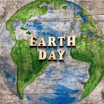 wood letters spell "earth day" on top of an image of the globe on a wood texture background