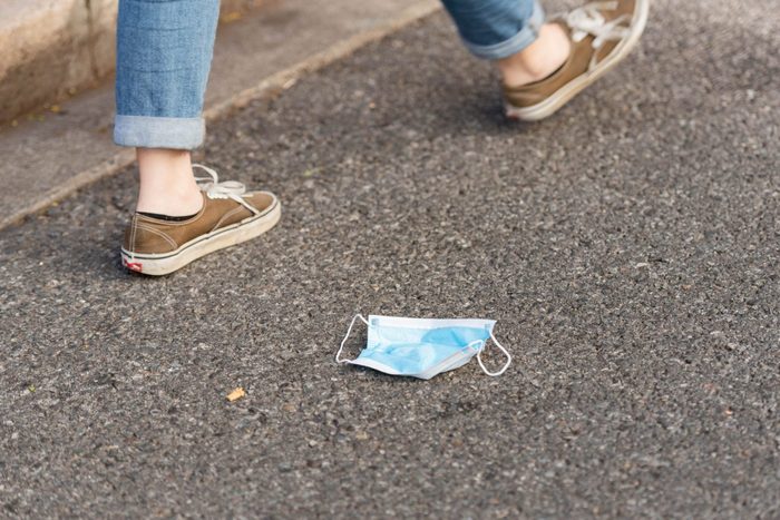 An anonymous pedestrian walks past a blue surgical face mask left on the ground.