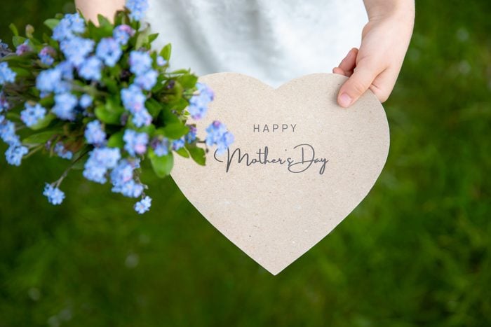 Happy Mother's Day written on a heart-shaped card and forget me nots held by a girl