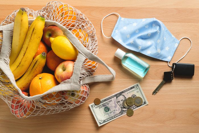 Dollar bills with cash coins, a protective medical mask, hand sanitizer, car keys. Eco-bag or string bag with organic farm products or purchases. Covid-19 and business concept. Prevention of the spread of the virus. Lifestyle attributes in a pandemic.