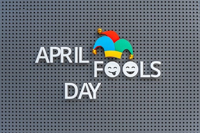 April Fools Day written on grey pegboard, jester hat decorates the lettering on gray background.