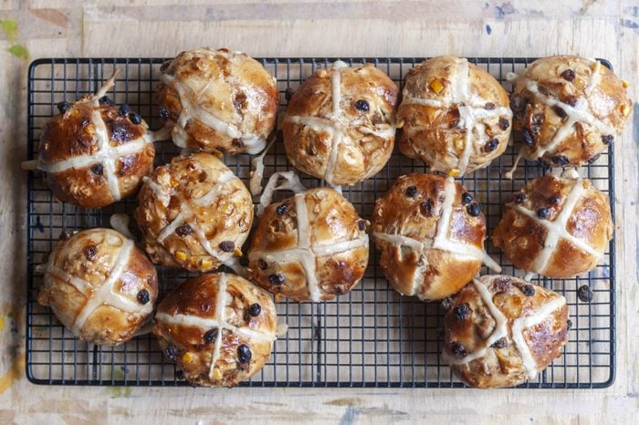 A close-up aerial view of freshly baked hot cross buns on a wire rack with a wooden surface beneath.