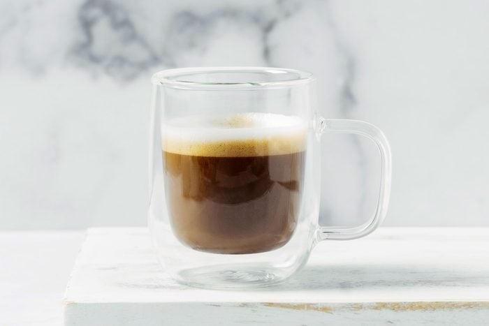 traditional espresso macchiato in a glass mug against a white marble background