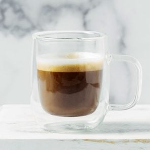 traditional espresso macchiato in a glass mug against a white marble background