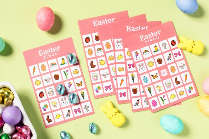 Printable Easter Bingo Cards arranged on a light green background surrounded by easter candy, chocolate eggs and peeps bunnies, and dyed easter eggs