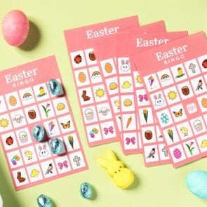 Printable Easter Bingo Cards arranged on a light green background surrounded by easter candy, chocolate eggs and peeps bunnies, and dyed easter eggs