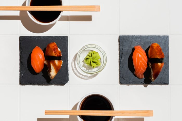 overhead view of a smal bowl of wasabi between two servings of sushi; soy sauce and chopsticks on the top and bottom of the frame