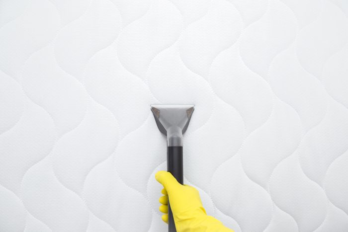 Hand with yellow glove cleaning a mattress with a vacuum