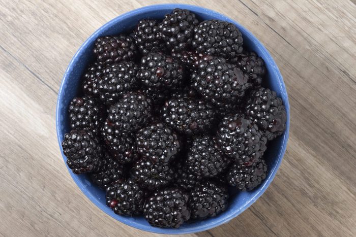 Ripe fresh blackberries in a bowl on a wooden table. Top view. Space for text.