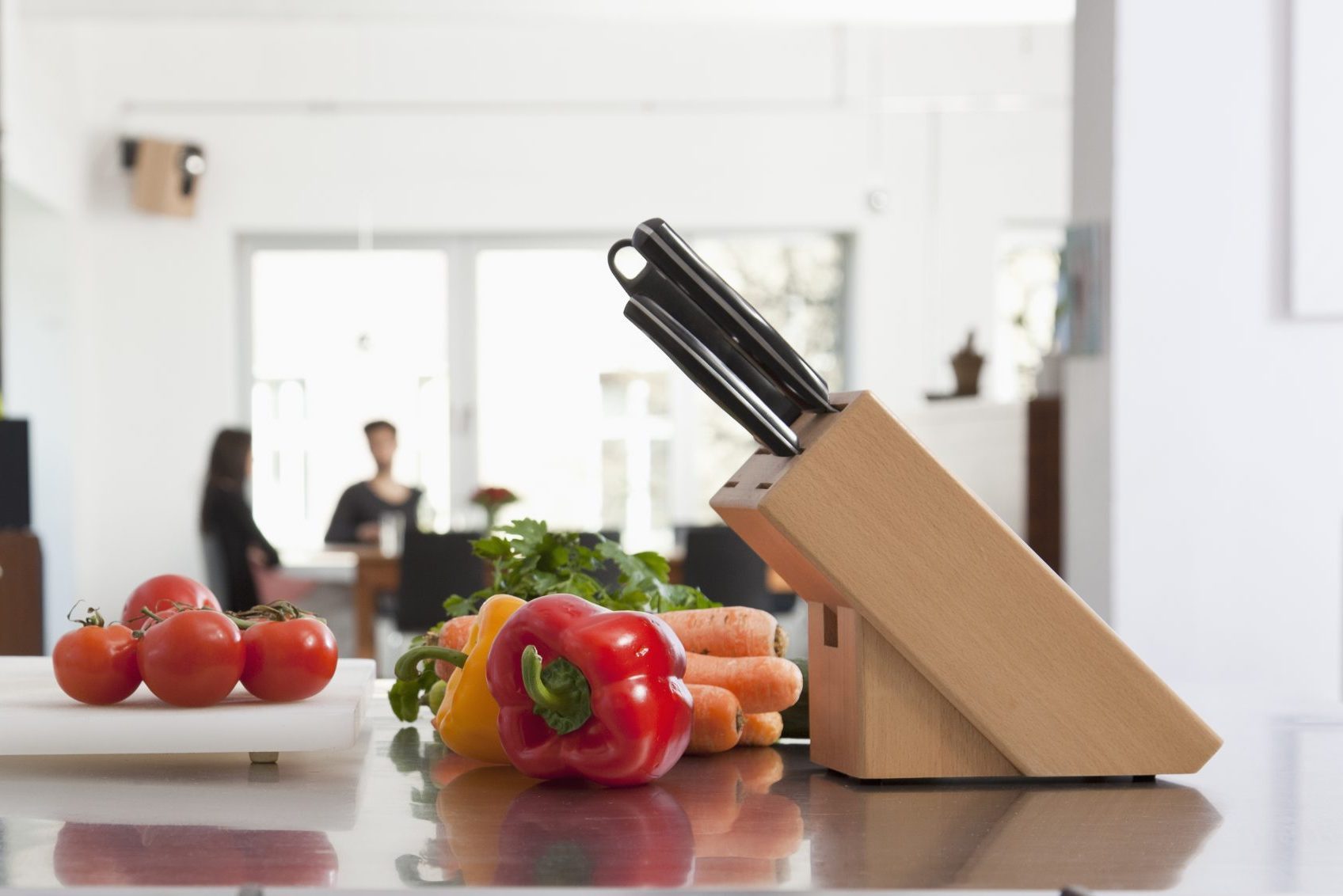 Tomatoes, carrots and bell peppers on a kitchen counter with knife block