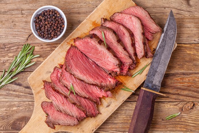 Sliced medium rare roasted beef meat on wooden cutting board, hunters knife
