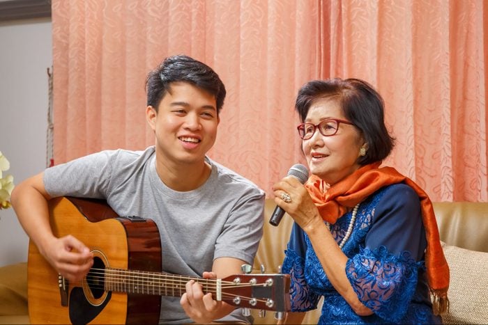 Adult son and senior mom sing a song while relaxed sitting on couch