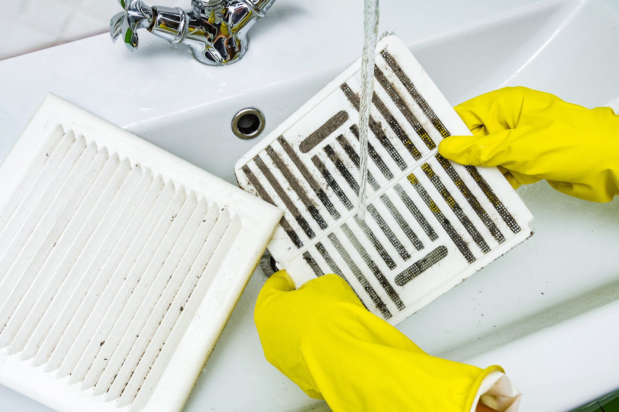 Person in a protective rubber glove washes a dusty bathroom vent in the sink