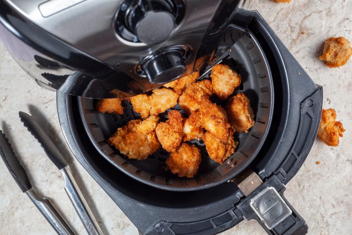 overhead view of open air fryer on a kitchen counter showing chicken bites, tongs nearby