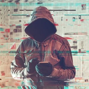 a hooded hacker person standing is using smartphone; the image is altered with a glitch effect