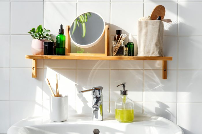 Toothbrush holder and other items on the edge of a bathroom sink with a shelf above