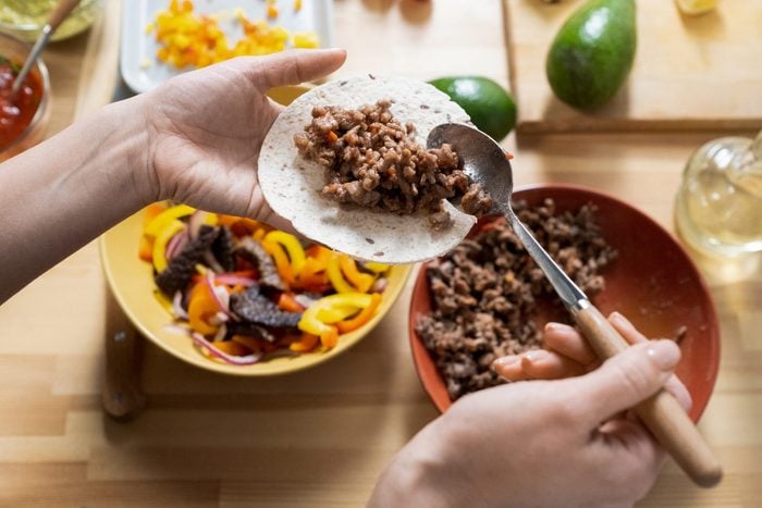 Hands of young woman with spoon putting fried minced meat on taco tortillas