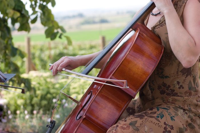 close up of woman playing cello with green vineyards behind her