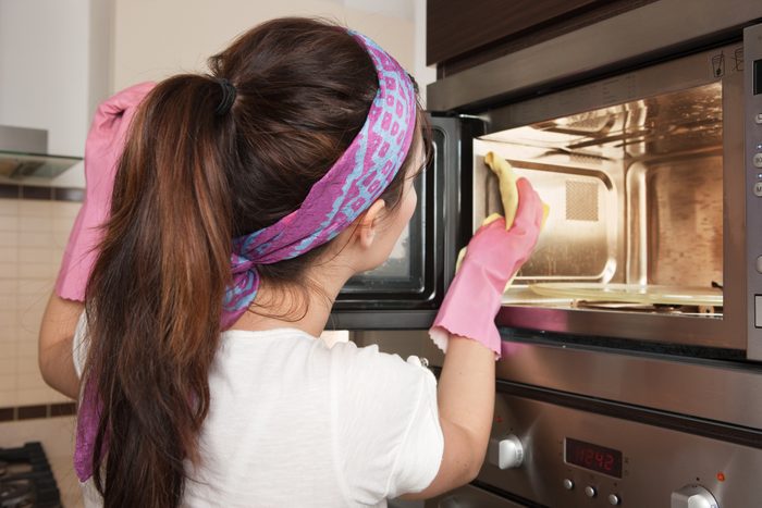 woman with brown hair Cleaning microwave in pink gloves