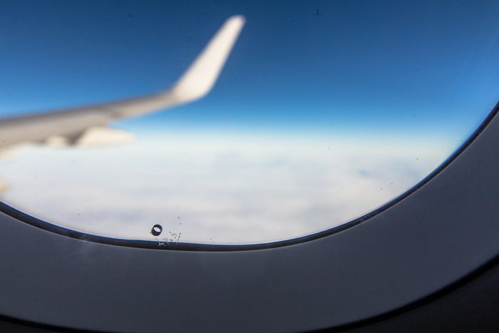 Airplane window breather hole bleed hole with wing blue sky
