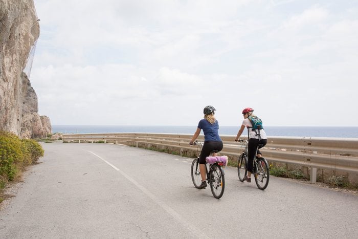 Mother and daughter bicycle along empty road, sea