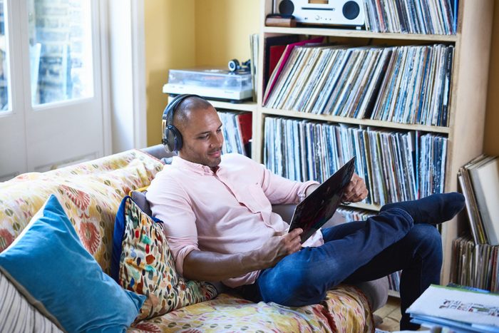 Man listening to a vinyl record and looking at the record cover on a couch at home