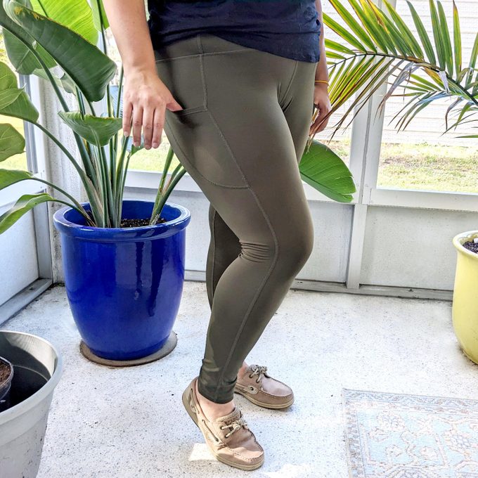 lower half of a woman in green leggings in a sunroom with plants