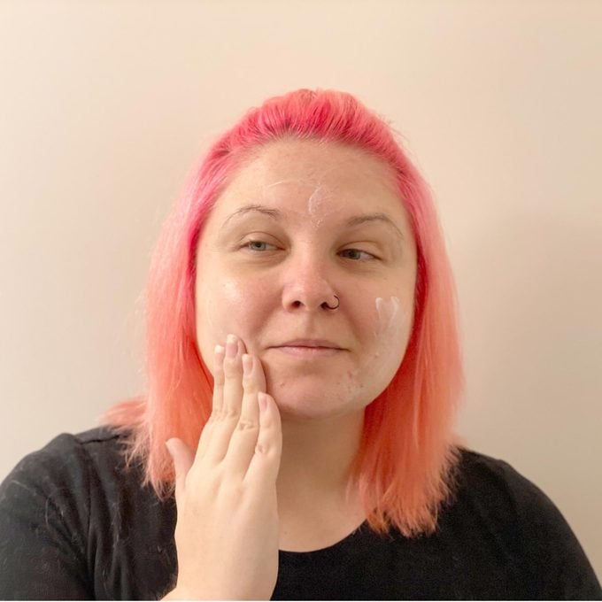 woman with pink hair applying moisturizer to her face