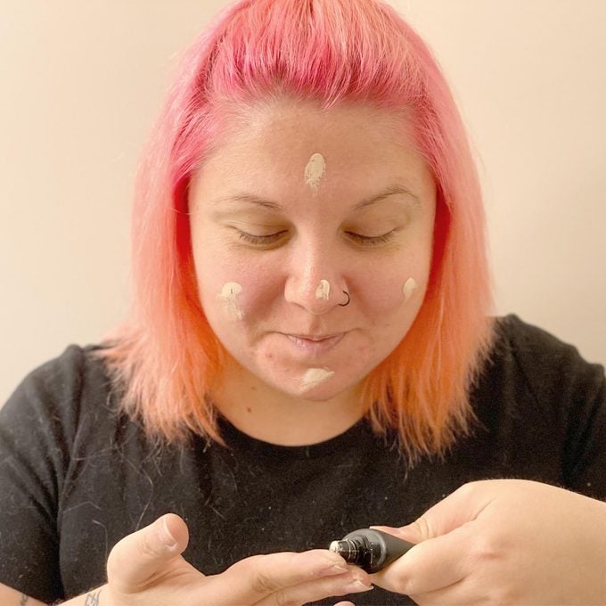 woman with pink hair applying primer to her face