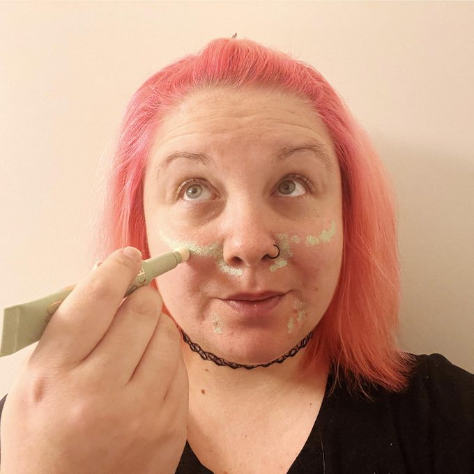 woman with pink hair applies color correct to her face to reduce redness