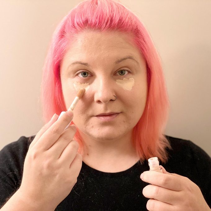 Woman with pink hair applying concealer under her eyes