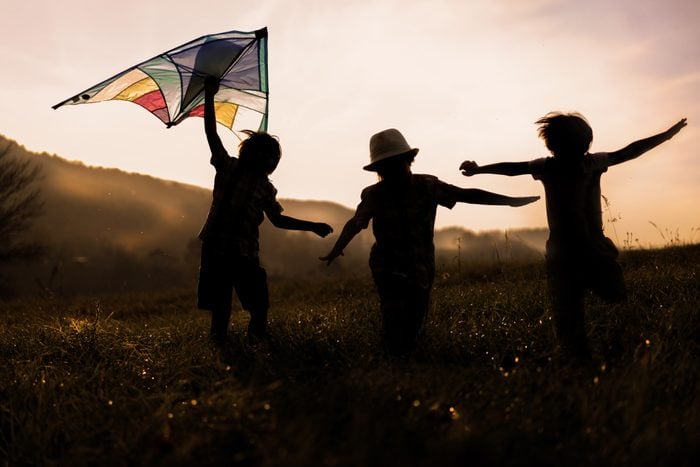 three happy children flying kites at sunset