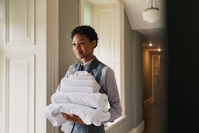 A side view of a woman working in a hotel, holding fresh towels for a hotel room.