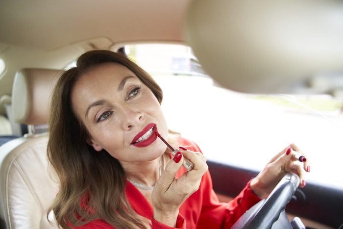Portrait of mature woman applying lipp gloss in car