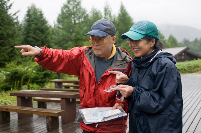 A senior guide guiding the way using compass with map to woman in Japan