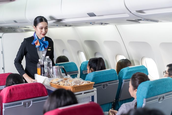 Asian female flight attendant serving food and drink to passengers on airplane
