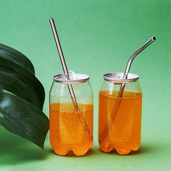 Cans with carbonated citrus beverage and reusable metal straws.Transparent tins with fizzy pop drink. Two jar with lemonade, on the green background.