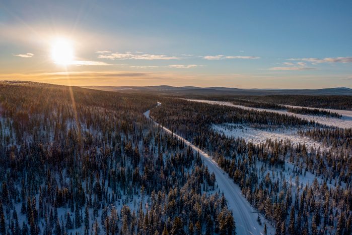 Snowy forest road with setting sun in Lapland, Finland