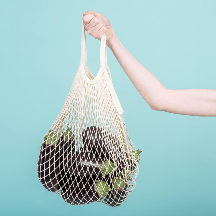 hand holding a reusable mesh produce bag filled with eggplants