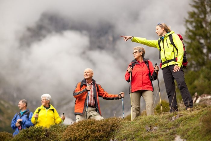 young female hiking guide showing senior group surrounding mount