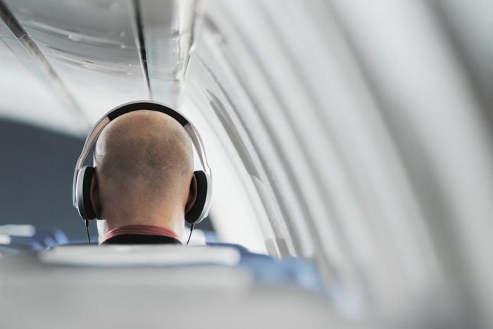 Businessman sitting on aeroplane seat, wearing headphones, rear view
