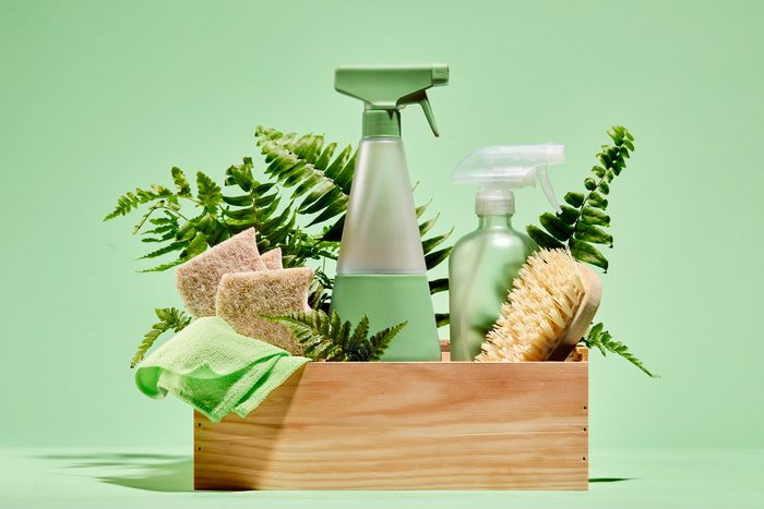 Green and natural cleaning products in a wooden box on a green background