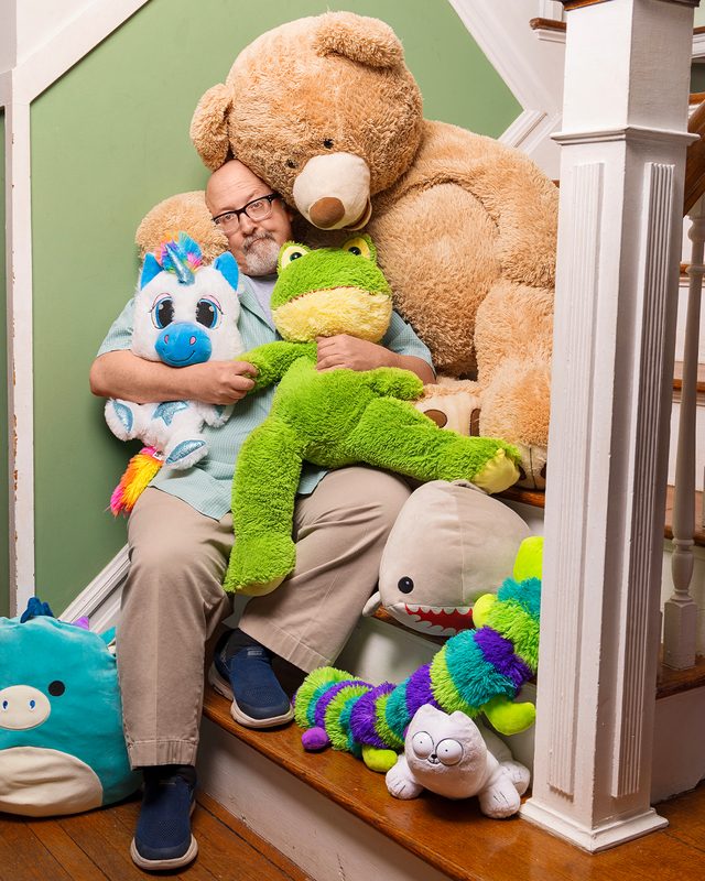 Dad hugging and posing with multiple oversized stuffed animals on a staircase at home