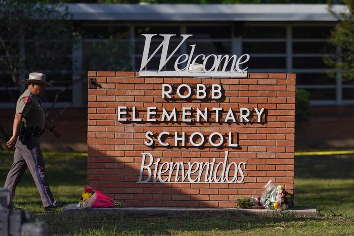 An officer walks outside of Robb Elementary School in Uvalde, Texas, on May 25, 2022. the school's sign has flowers laid on the bottom.