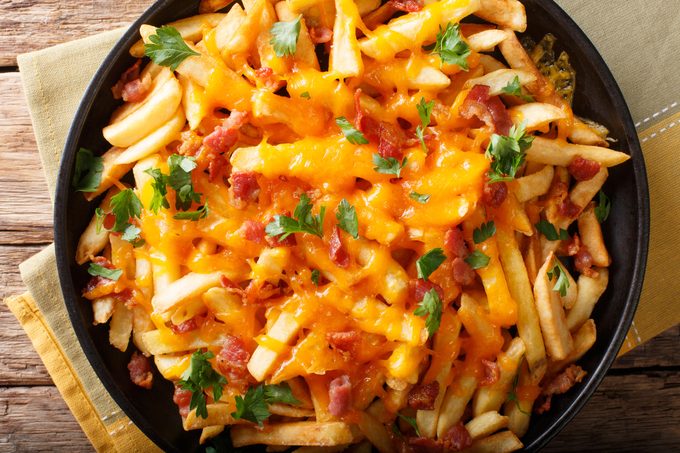 French fries with cheddar cheese, bacon and herbs close-up