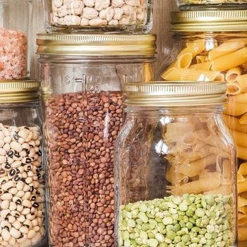 Shelf in the kitchen with various cereals and seeds - peas split, sunflower and pumpkin seeds, beans, rice, pasta, oatmeal, couscous, lentils, bulgur in glass jars