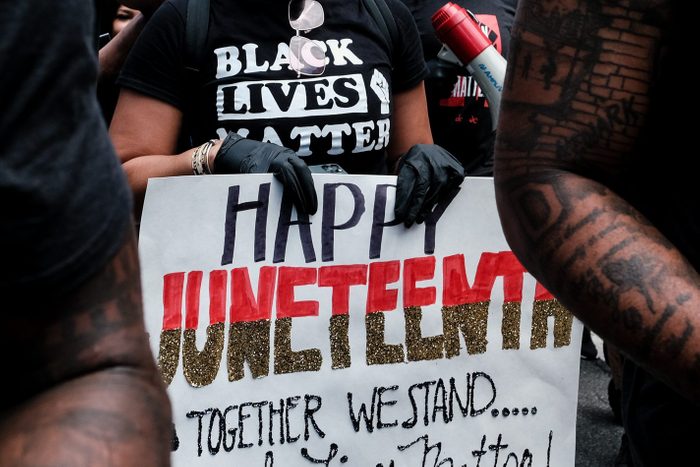 hands holding a handmade sign that says 'Happy Juneteenth' and 'together we stand' below it